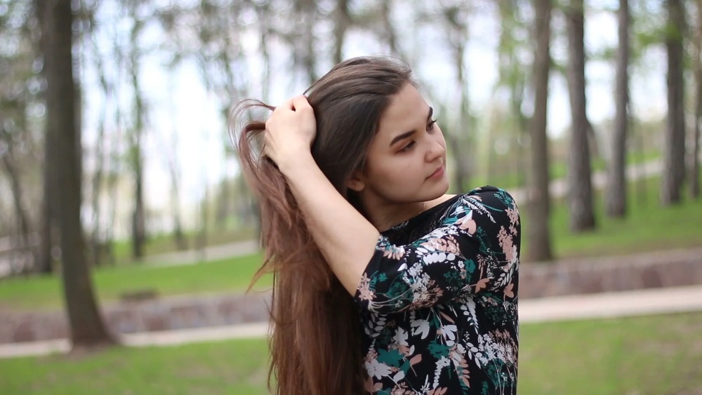 Chica en el parque tocándose el cabello con su mano
