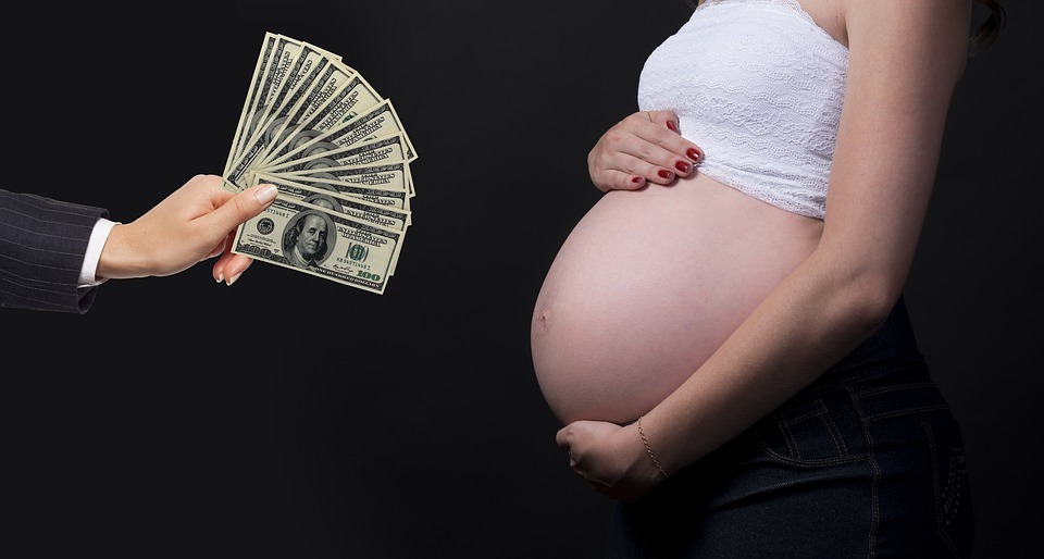 Mujer embarazada con la barriga descubierta y la mano de un hombre con dólares